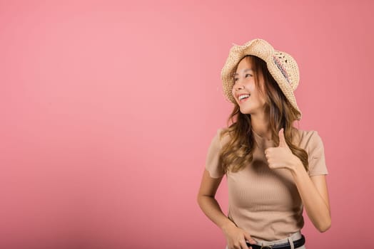 Portrait Asian young woman is smiling and giving a thumbs up while wearing a hat in studio shot isolated pink background, which gives it a cheerful and positive vibe, excellent sign
