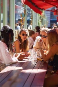 A group of stylish women chatting at a sunlit outdoor cafe, enjoying conversation and drinks. Perfect for visuals highlighting female friendship, summer lifestyle, and relaxed urban scenes