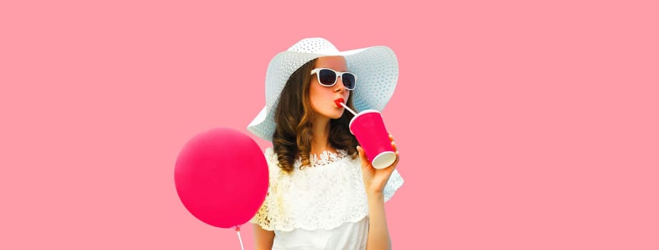 Portrait of beautiful young woman model with cup of coffee or fresh juice holding balloon wearing white summer straw hat on pink studio background