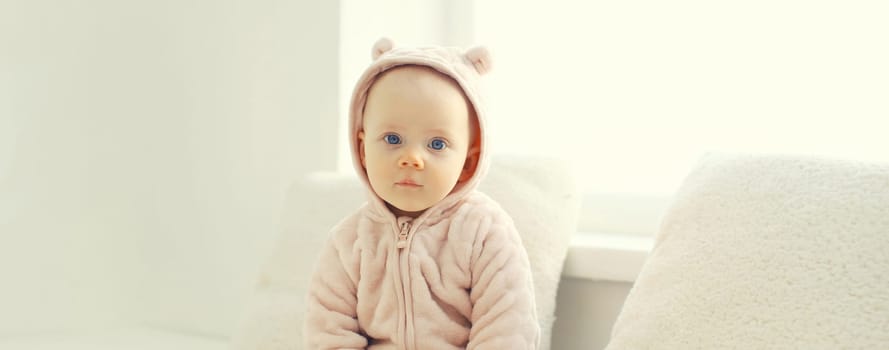 Cute little baby sitting on the floor in bathrobe in white room at home near window