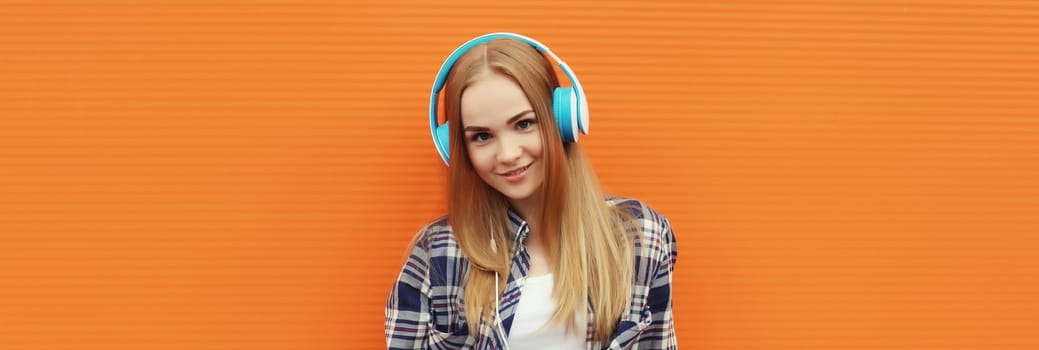 Summer portrait of happy modern young woman listening to music with headphones on orange wall background