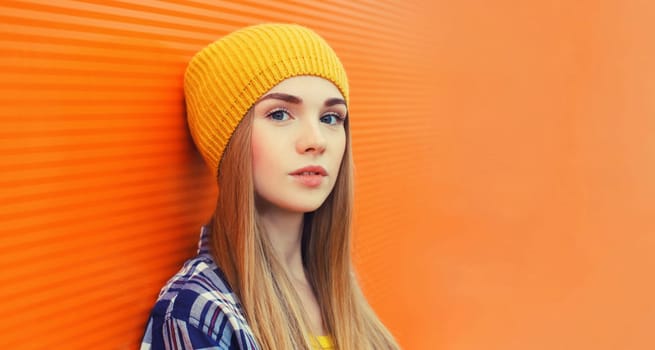 Portrait close up of modern young teenage blonde girl in yellow hat looking at camera on a summer day on orange background