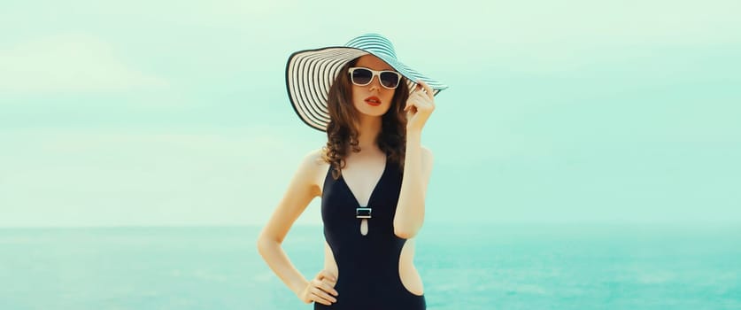 Summer vacation, beautiful young woman in bikini swimsuit and black straw tourist hat, stylish girl posing on the beach on sea coast background