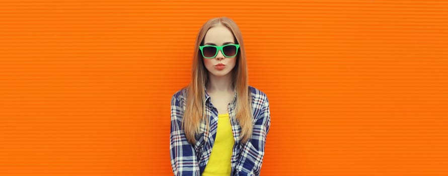 Summer portrait of happy cheerful stylish young woman, teenager girl in colorful clothes, glasses posing on orange background on city street