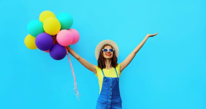 Summer happy smiling young woman with bunch of colorful balloons having fun having fun wearing straw hat on blue studio background