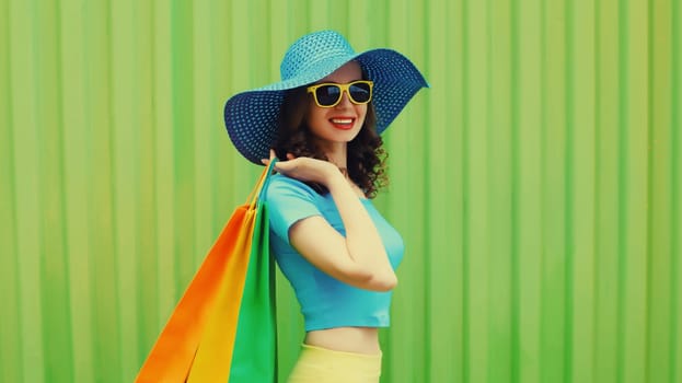 Fashion, purchase. Stylish beautiful happy young woman posing with colorful shopping bags, girl in summer hat standing on bright green background