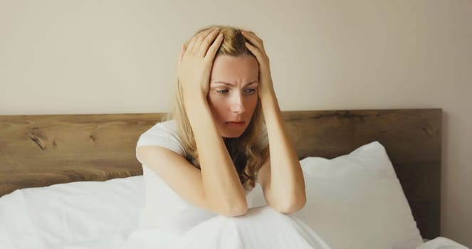 Exhausted tired woman touching head, suffering from headache, stress, fatigue, temples pain, migraine, loud noise, tension lying on the bed in bedroom at home