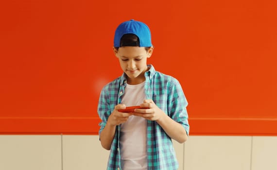 Happy modern teenage boy with phone, kid holding smartphone in the city on colorful red wall background