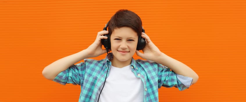 Portrait of happy modern teenage boy listening to music with headphones in the city on orange wall background