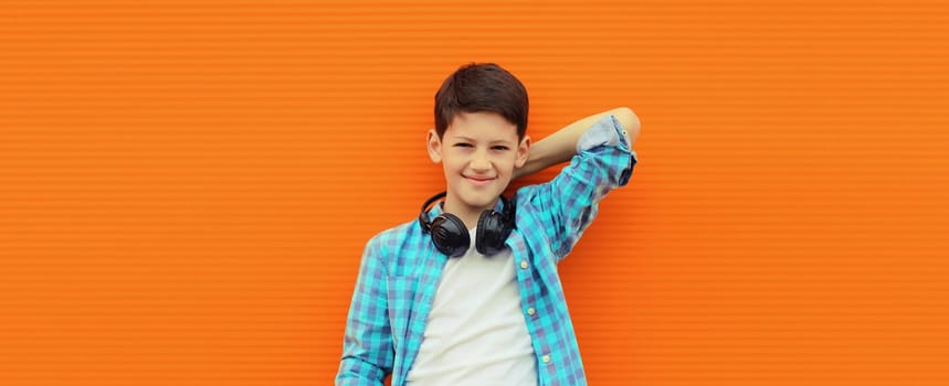Portrait of happy modern teenage boy listening to music with headphones in the city on orange wall background
