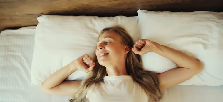 Happy young woman sleeping lying in bed on white soft comfortable pillow in bedroom at home