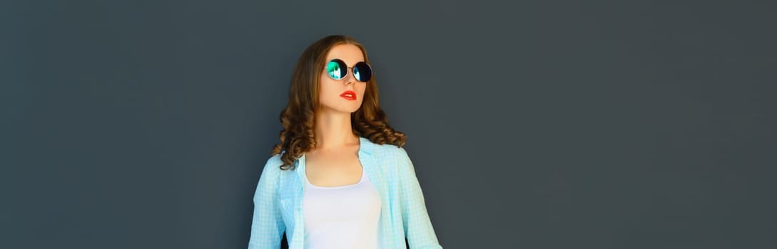 Portrait of stylish modern young woman in glasses, posing on black wall background