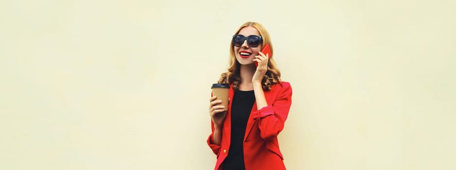 Beautiful young woman calling on smartphone in red business suit with coffee drink cup isolated on white background