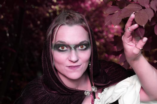 A woman dressed as a red forest spirit or witch looks out of the bushes