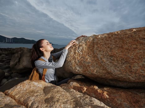 A young woman in active wear climbs large rocks by the ocean, embodying a spirit of exploration and adventure The cloudy sky and coastal scenery enhance the atmosphere of determination and excitement