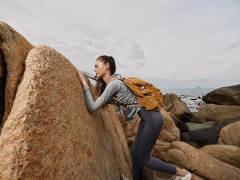 A determined young woman, wearing athletic attire and a backpack, climbs rocky terrain by the sea, embodying adventure, exploration, and resilience in nature