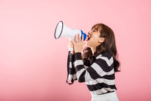 Portrait of happy Asian beautiful young woman teen confident smiling face holding making announcement message shouting screaming in megaphone, studio shot isolated on pink background, with copy space