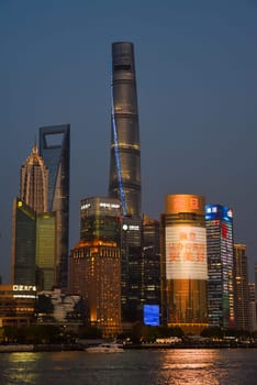 Shanghai, China - 1 April 2025: Evening skyline of Pudong district featuring illuminated Shanghai Tower, Shanghai World Financial Center, and Jin Mao Tower reflected in Huangpu River