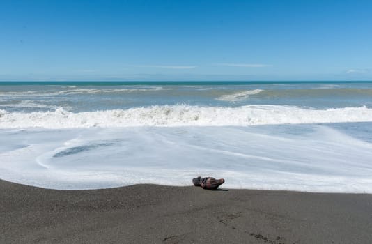 Waves crash onto South Pacific beach lined with cliffs bin New Zealand leading white foam wash as they flow back.