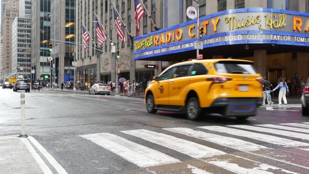 New York, United States - 10 Sept 2023: Manhattan Midtown street. Radio City Music Hall, Rockefeller Center, USA. People pedestrian, urban traffic, 6 Sixth Americas avenue crossroad, yellow taxi cab.