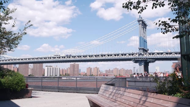 New York City, United States - 30 Aug 2023: Cable-stayed Manhattan Bridge to Brooklyn Dumbo. Bench on Time Out Market rooftop, iconic United States travel destination. People on NYC roof vista point.
