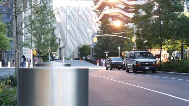 New York City, United States - 1 Sept 2023: Hudson Yards Vessel architecture in Chelsea, Manhattan Midtown, NYC, USA. NYPD police patrol car. People on urban road, 34 street. Sunset rays reflection.