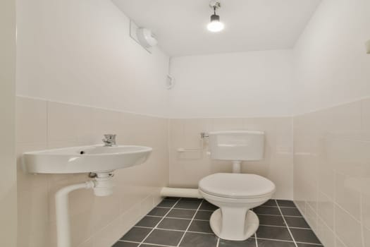 A clean, minimalist bathroom featuring a white wall-mounted sink and a modern toilet, complemented by sleek tiles and efficient lighting.