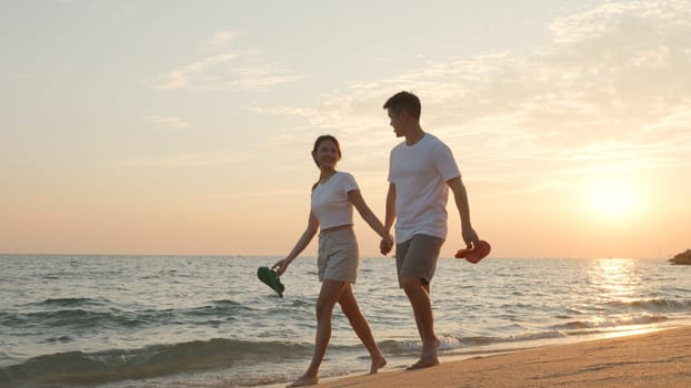 Vacation loving couple walking on beach together at sunset landscape, relaxing vacation travel summer, Asian man and woman in love holding hands walks along the sandy seashore
