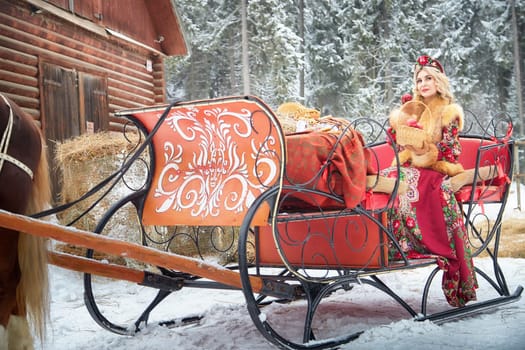 A gorgeous Russian girl in colorful attire poses with a horse during Maslenitsa, celebrating winter.