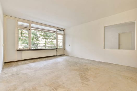 An empty room showcasing a minimalist design with large windows allowing natural light. The flooring and walls are simple, emphasizing space and openness.