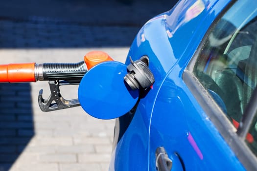 A blue car is currently being filled with gasoline at a busy gas station, ensuring it has enough fuel for its next journey ahead