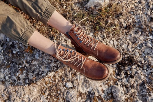 Exploring the wilderness person's feet in brown boots on rocky surface with grass and rocks in background