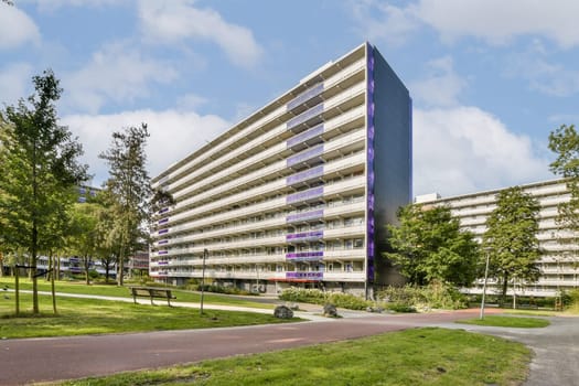 A striking modern residential building featuring multiple floors with large windows, set amidst beautifully landscaped greenery and pathways.