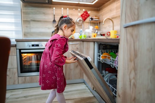 A young girl in a charming dress engages in household chores, opening the dishwasher in a sleek kitchen filled with colorful dishes. Sunlight pours in, adding warmth to the setting.