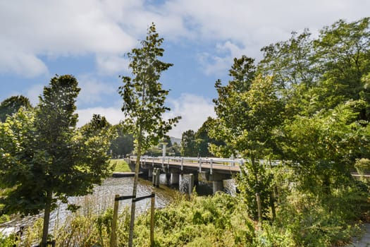 A picturesque view of a bridge spanning a calm body of water, surrounded by lush greenery and a clear blue sky, inviting tranquility and exploration.