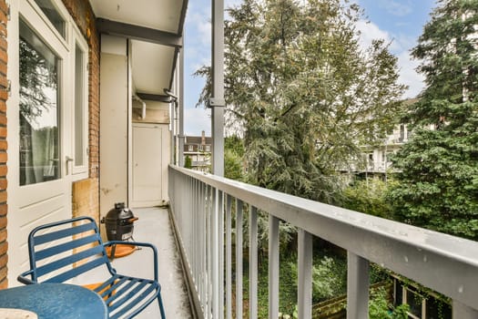 A peaceful balcony scene features blue chairs and a serene view of lush trees and a nearby building in the background, inviting relaxation.