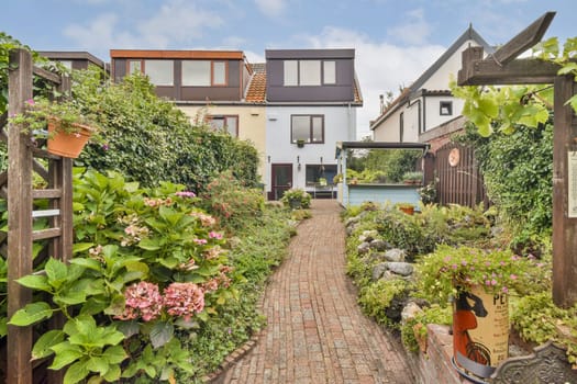 A picturesque view of a garden pathway lined with blooming flowers, leading to modern houses with glass windows, showcasing tranquility and charm in a residential area.