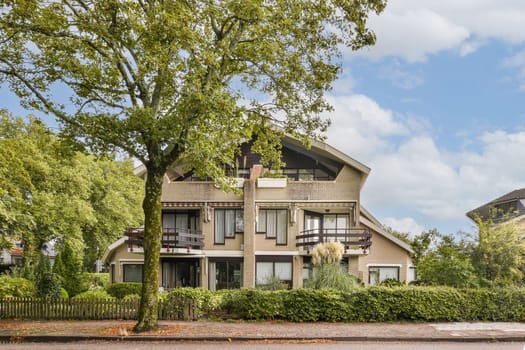 A contemporary house featuring large windows and balconies, nestled among lush trees and landscaped gardens, providing a serene living environment.