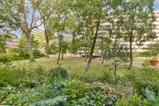 Vibrant greenery fills the scene, showcasing trees and plants in a tranquil urban park setting. The sunlight filters through the foliage, creating a serene atmosphere.