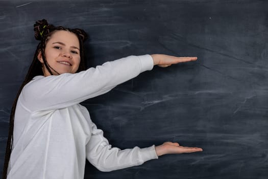 A cheerful, smiling girl is playfully gesturing in front of a large black chalkboard background, full of creativity