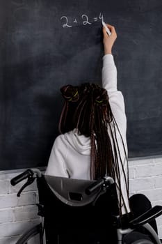 A determined individual in a wheelchair writes on a chalkboard, showcasing empowerment and accessibility.