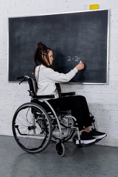 A young woman, who uses a wheelchair, engages in a creative activity at a chalkboard within a modern classroom