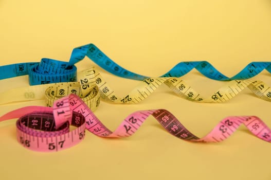 Side view of pink, yellow and blue tape measure on yellow background with customizable space for text. Dieting concept and copy space.