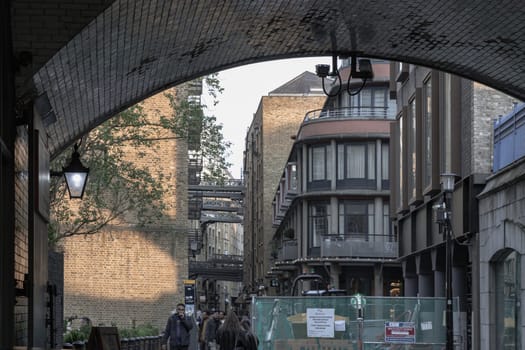 London, UK - Apr 27, 2025 - A view from under Tower Bridge, Pedestrians walking on Shad Thames is a historic riverside street alongside converted warehouse complex and shops under bridges in London. use it as your Wallpaper, Poster and Space for text, Selective focus.