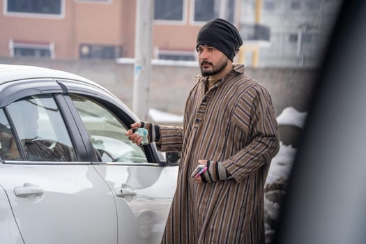 Srinagar, Kashmir - 4th Jan 2025: Young islamic man in traditional phiran and headgear collecting money at the parking toll helping in the efficient running of the road network