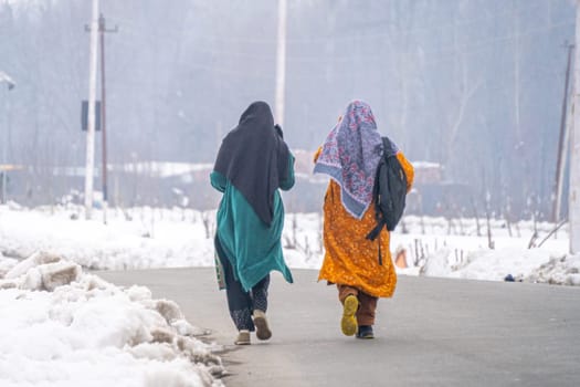 Srinagar, Kashmir - 4th Jan 2025: Woman in traditional kashmiri clothing of salwar kameez walking along a snow covered road in the middle of the harsh winter of the region