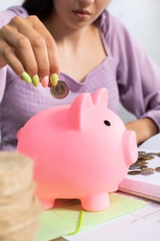 A woman deposits shiny coins into a pink piggy bank, symbolizing her savings and thoughtful financial planning