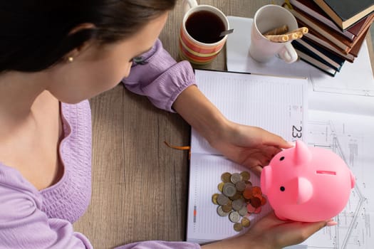 A woman is thoughtfully analyzing her savings with a cheerful piggy bank, surrounded by notes and a warm cup of coffee