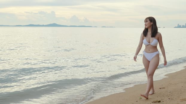 Young beautiful woman wearing bikini swimsuit walking smiling resting relax along on tropical white sand beach, Happy Asian female walk holiday outside, Summer travel vacation concept