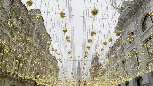 Festive atmosphere in moscow with golden decorations illuminating nikolskaya street, featuring the kremlin tower in the distance
